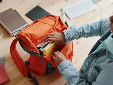 A primary-aged pupil sitting at a desk with school materials spread out, focusing on organising their work in a calm classroom environment.