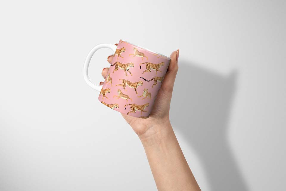 Thumbnail: Leopard Mug in Pink 11oz, leopard pattern print, with leaping leopard, pink coral background, mug held up in hand