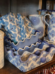 Shelf display of blue-and-white patterned ceramic mugs and bowls stacked together.