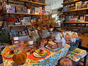 Table display of orange floral arrangements, pumpkins, and colorful patterned linens.