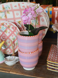 Shelf display of pink patterned planters and plaid ceramic items.