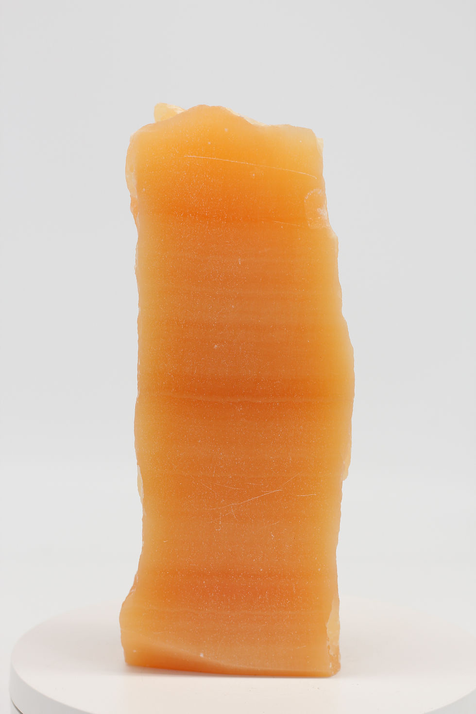 Slanke oranje calciet kristalzuil met horizontale groeilijnen op wit plateau 16cm ORCA003