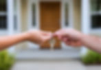 Close-up of new homeowner receiving house keys in front of modern home, symbolizing residential property ownership