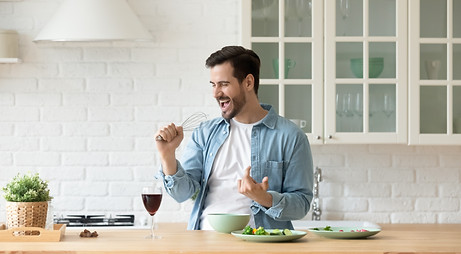 Funny young man singing song into whisk, cooking in modern kitchen, happy male holding kit