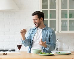 Funny young man singing song into whisk, cooking in modern kitchen, happy male holding kit