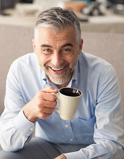 Man relaxing at home on the couch and having a coffee break, he is smiling at camera and h