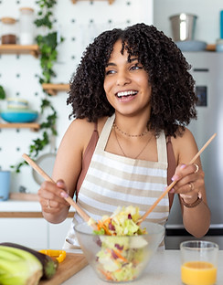 Close up photo of a smiling young woman makes a fresh vegan salad while she uses olive oil