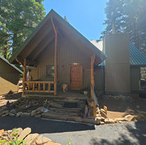 Front elevation of the Heidi Way cabin showing the original entry deck with deteriorated peeled-log stairs before repair.