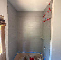 Tub surround tile set on three walls with leveling clips still in place and the tub protected