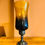 Thumbnail: Tall hurricane candle holder with an amber to dark blue/black ombre glass shade and a rustic dark metal pedestal base
