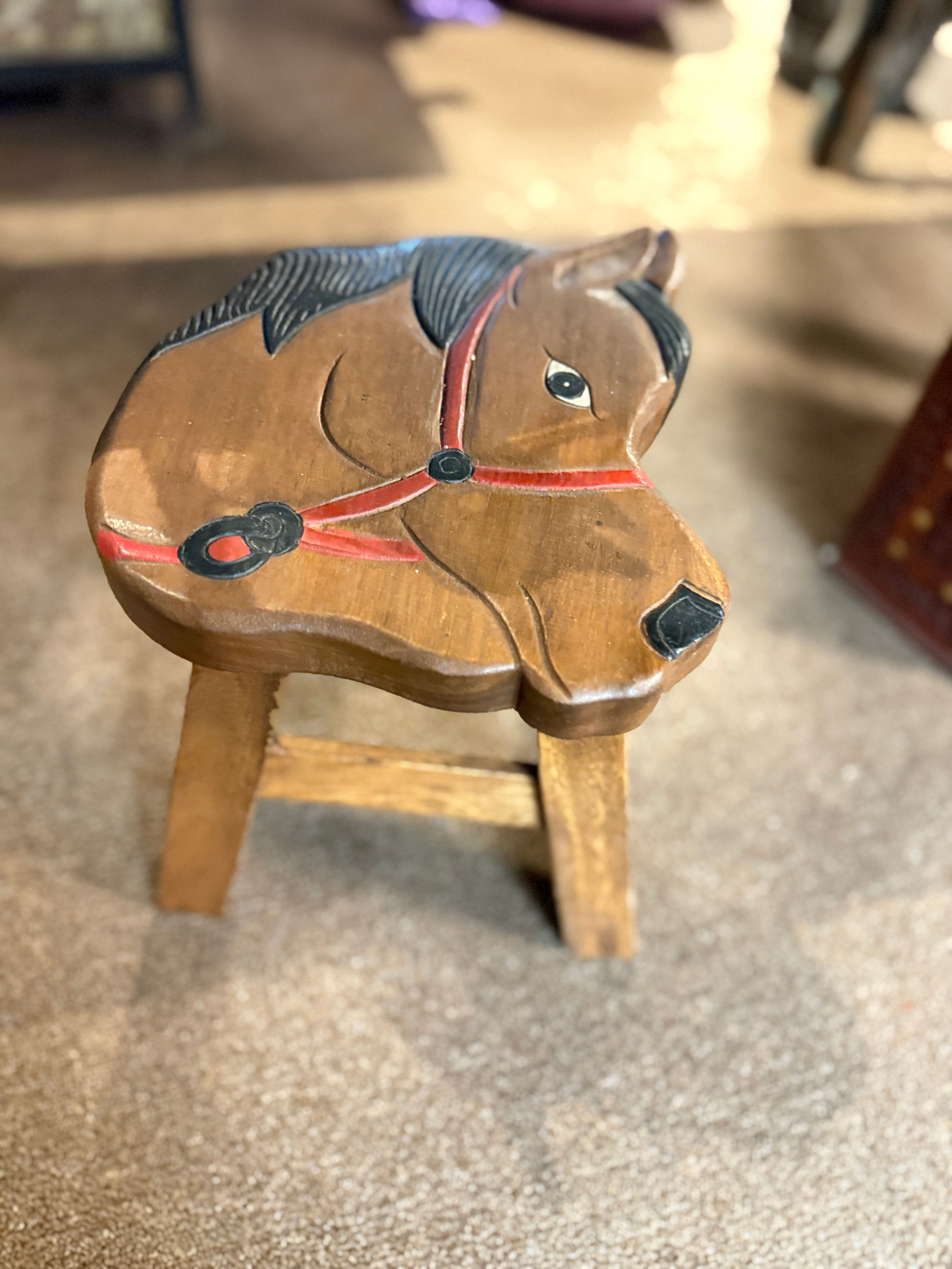 Light brown hand-carved wooden stool with a seat shaped like a horse's head, featuring black mane details