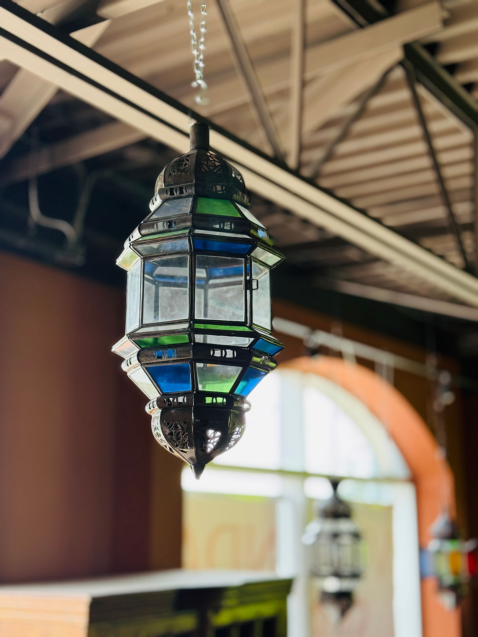 Thumbnail: Ornate Moroccan-style hanging lamp with a dark metal frame, featuring a mix of clear, green, and blue stained glass panels