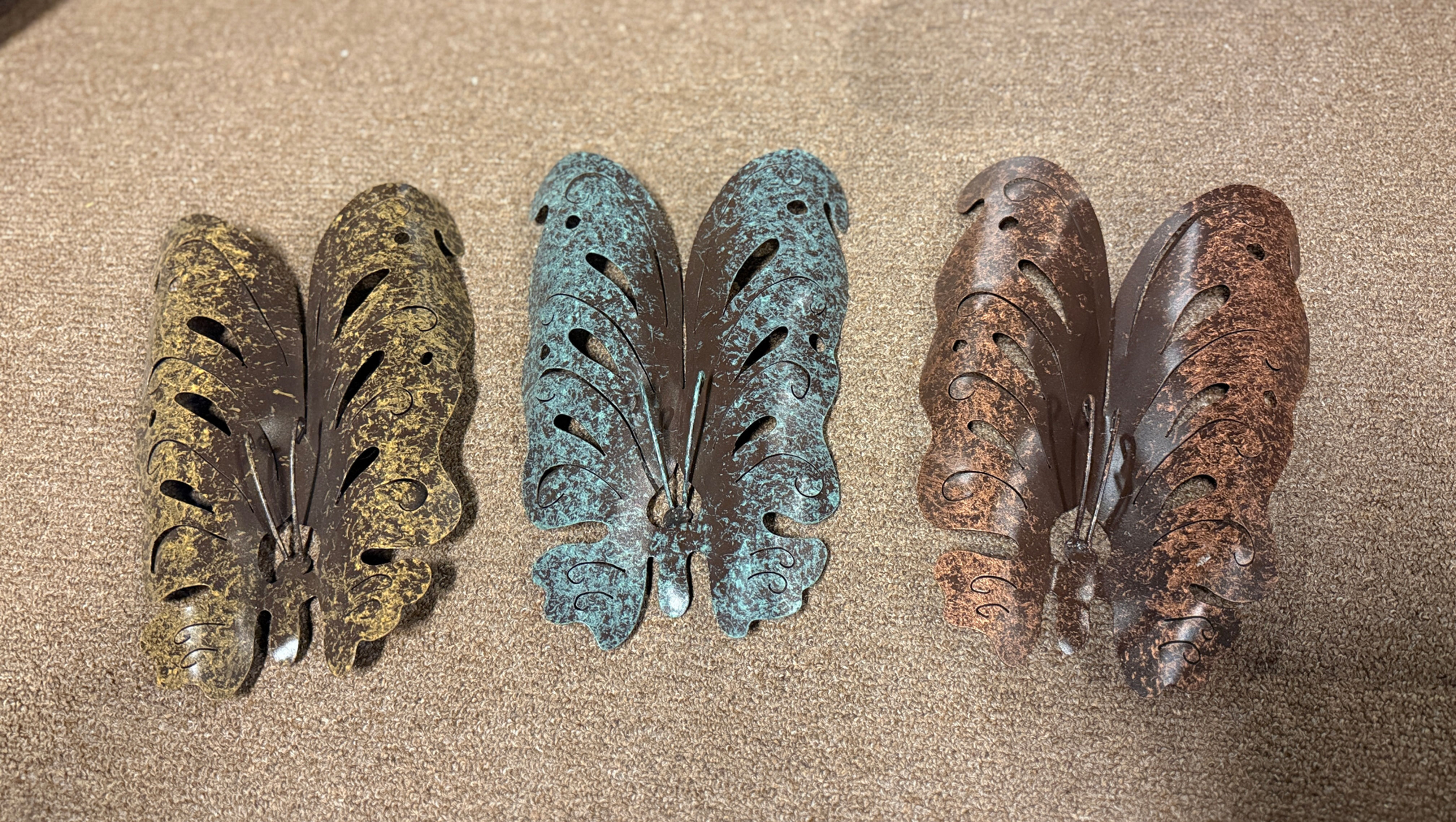 Three decorative metal butterfly sculptures in a row, each with a different rustic patina finish