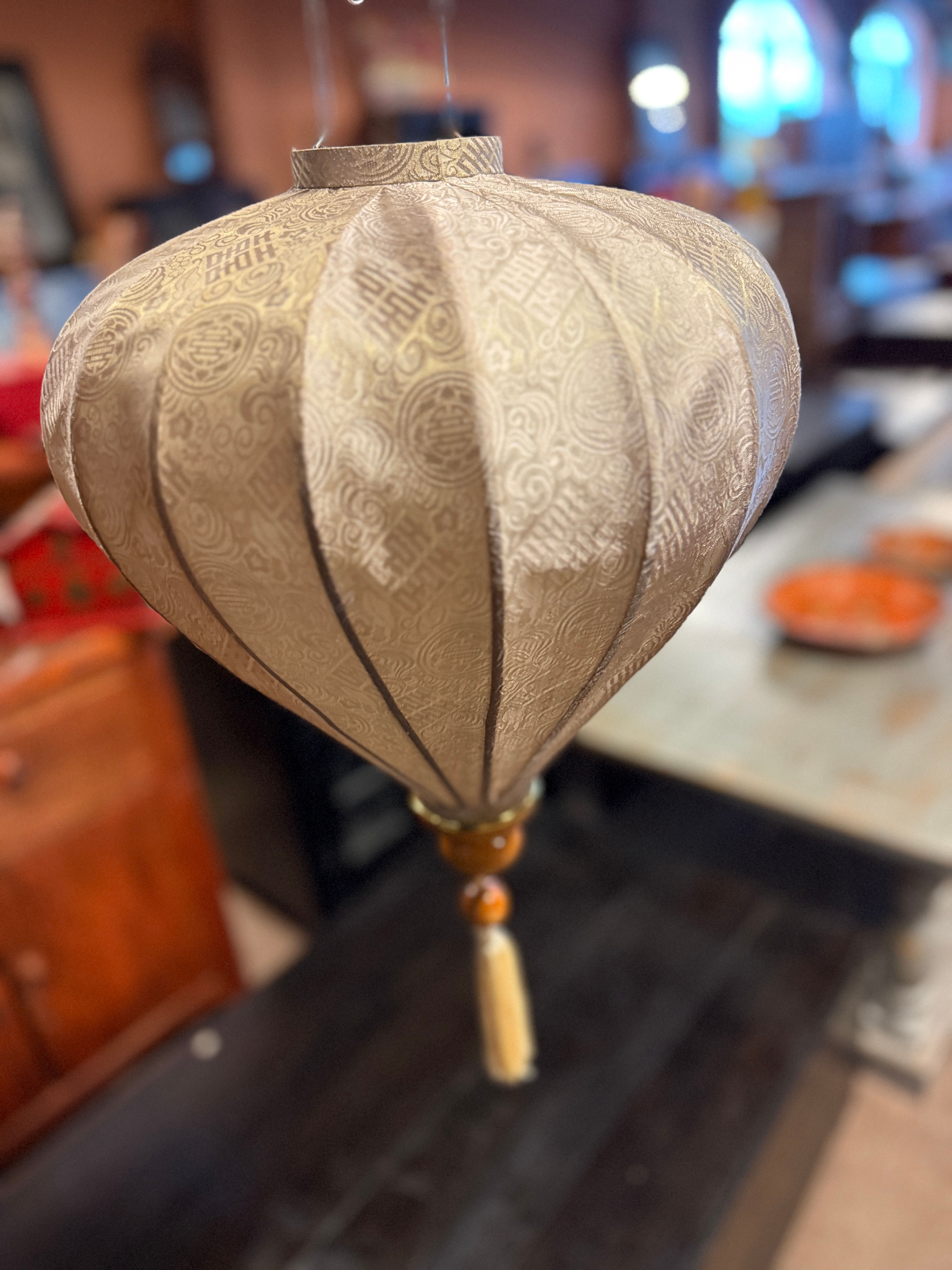 Light gold silk hanging lantern with a subtle woven brocade pattern of traditional symbols