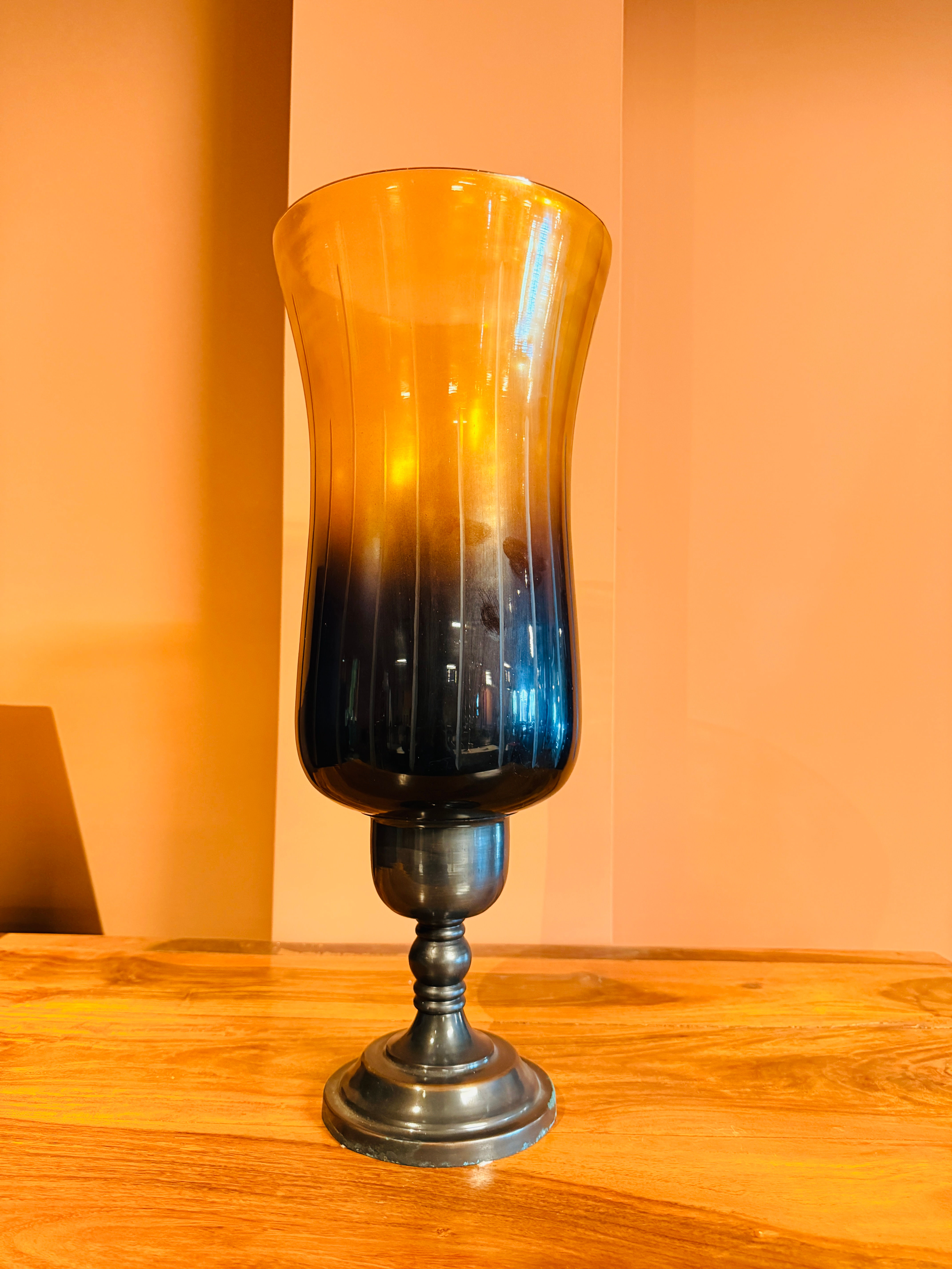 Tall hurricane candle holder with an amber to dark blue/black ombre glass shade and a rustic dark metal pedestal base