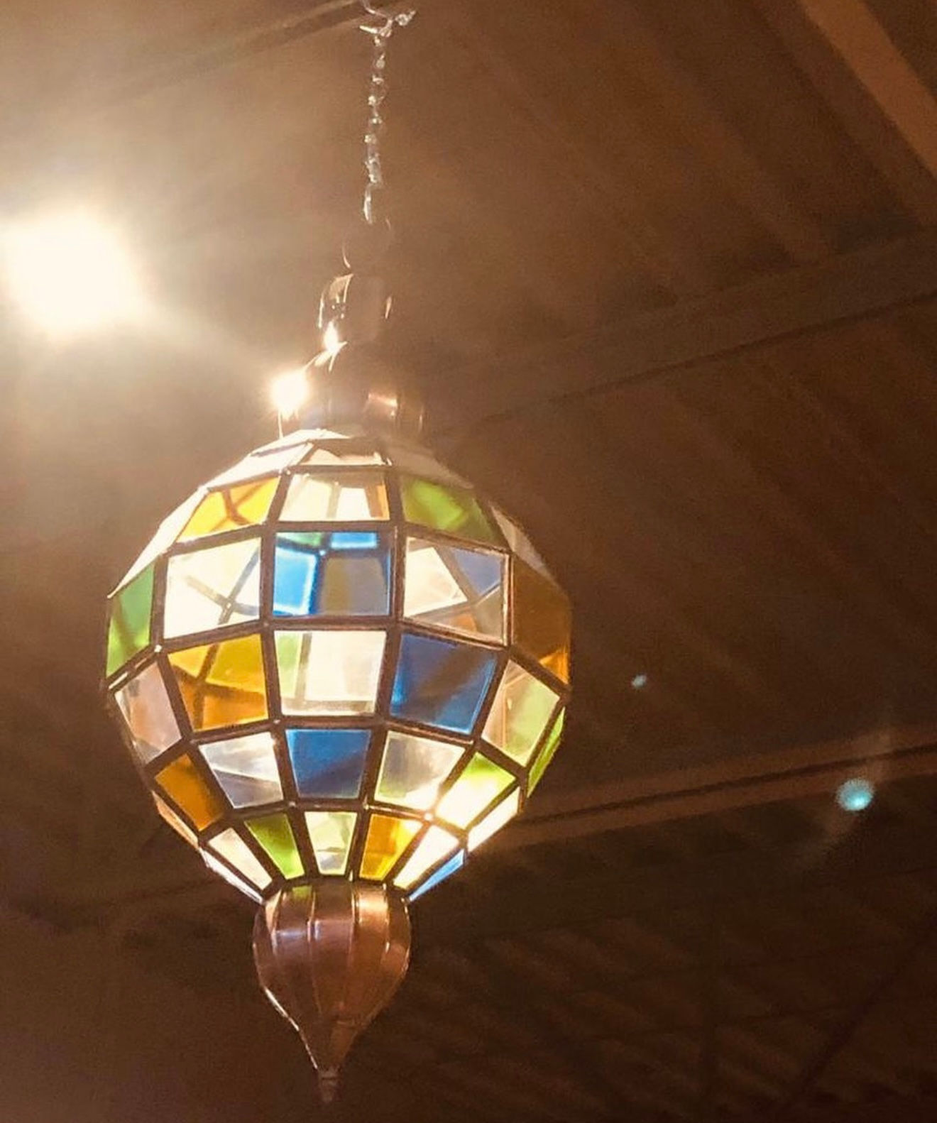Vintage Moroccan-style globe pendant light with a mosaic of multi-colored stained glass panels in  emitting a warm glow.