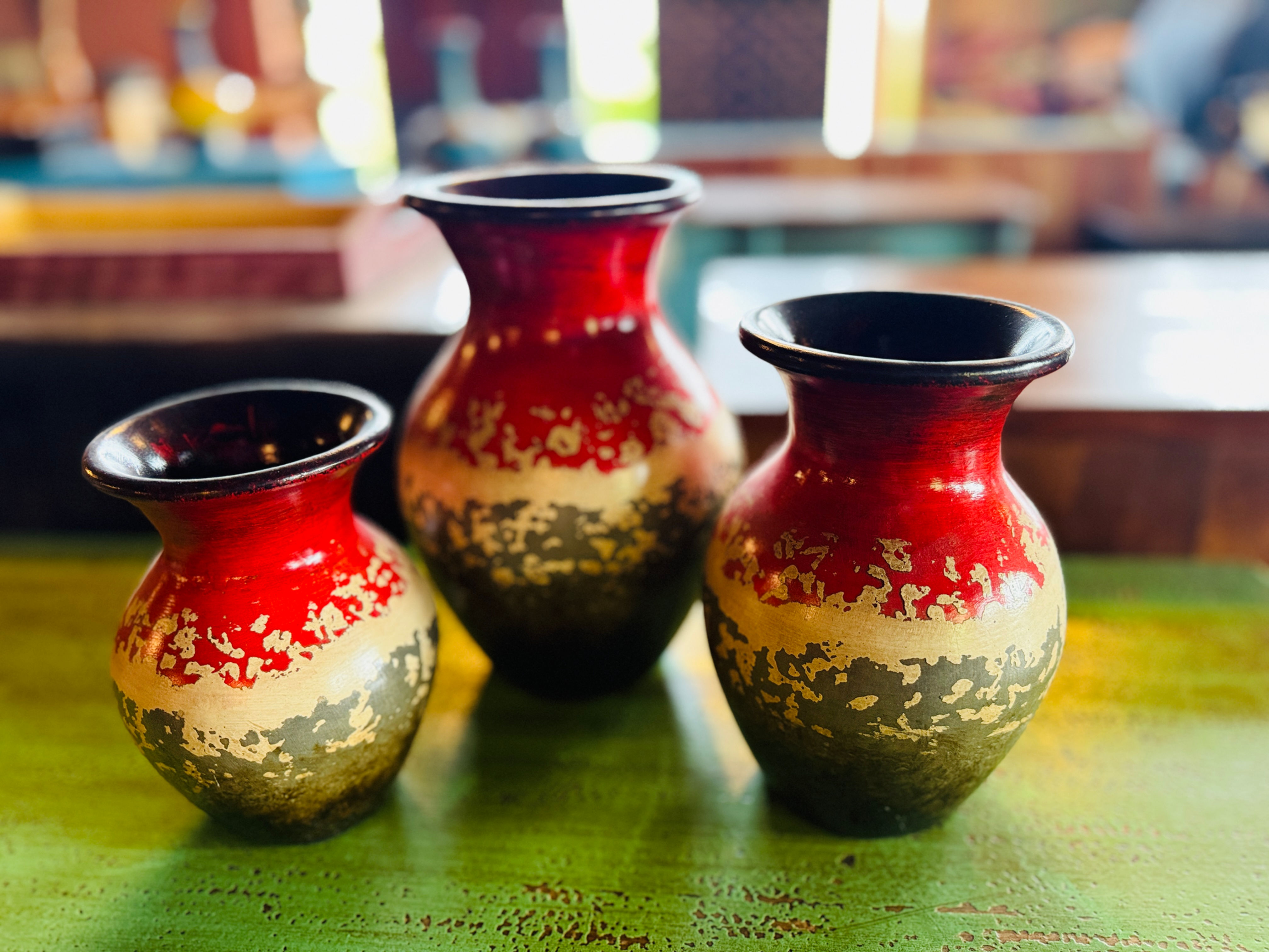 A set of three hand-painted ceramic or clay vases in varying sizes, featuring a vibrant red top half with distressed gold