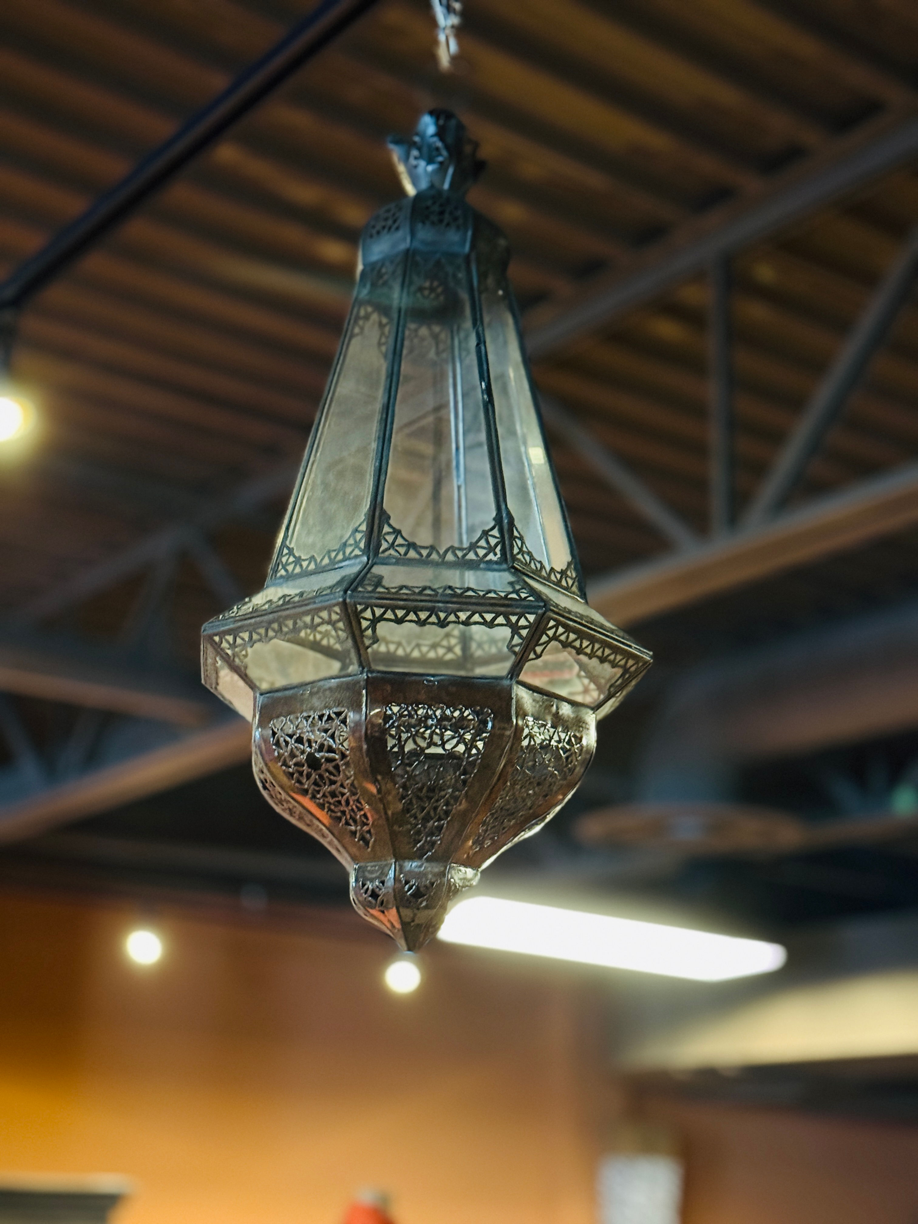 Large, ornate Moroccan-style hanging lantern with a lear glass panels and intricate geometric perforated metalwork.