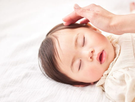 眠っている赤ちゃんの頭にやさしく触れる様子。頭の形や向き癖に関係する日常のケア