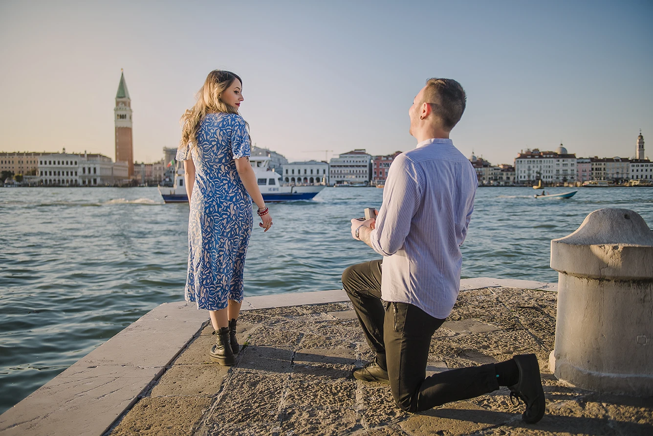 Barth unexpectedly gets down on one knee in San Giorgio Maggiore, presenting an engagement ring to a surprised Maria, whose hands cover a joyful smile.