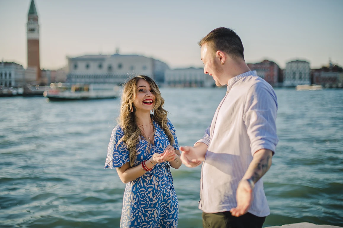 Close-up of Maria's hands as she lovingly touches Barth's shoulder while looking down at the ring with teary eyes of happiness against the backdrop of the Venice lagoon.