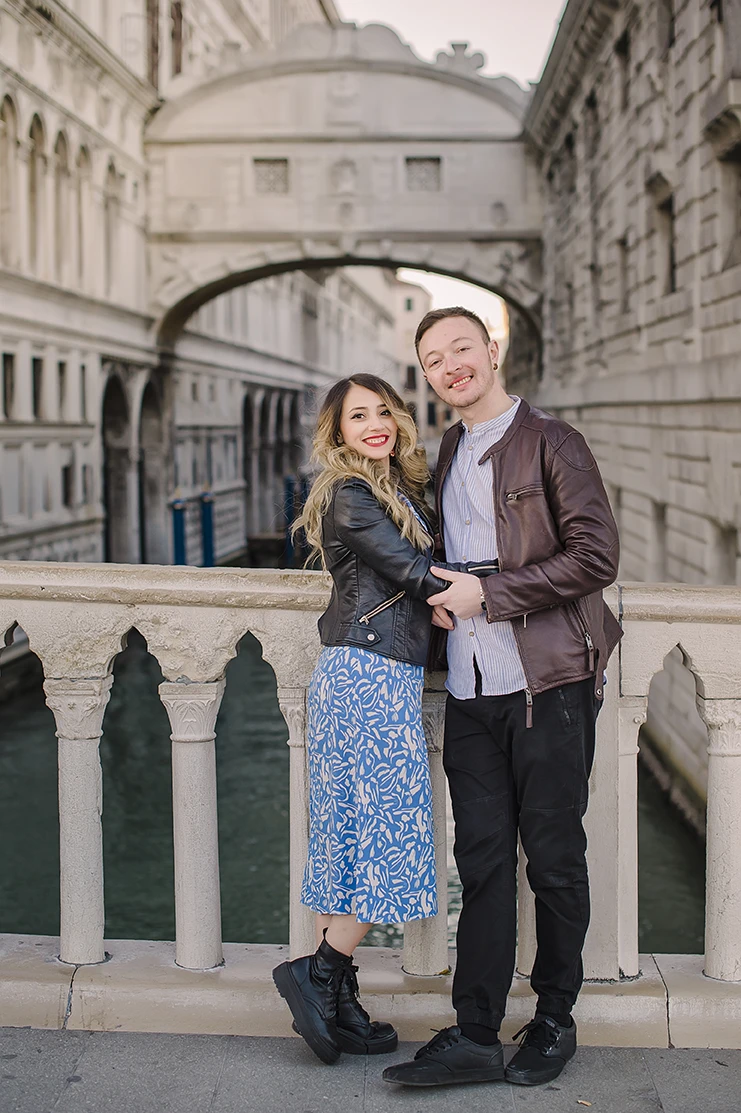 A candid shot capturing the couple's spontaneous dance, with Maria's flowing dress and the serene, amber-tinted sky of Venice creating a timeless scene.