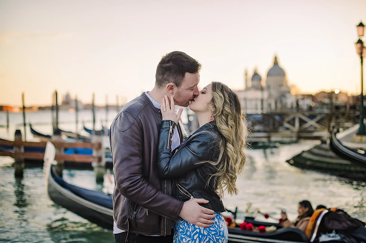 Laughing together, Maria playfully places her engagement ring-adorned hand on Barth's chest as they savor the moment, a gondola leisurely drifting in the background.