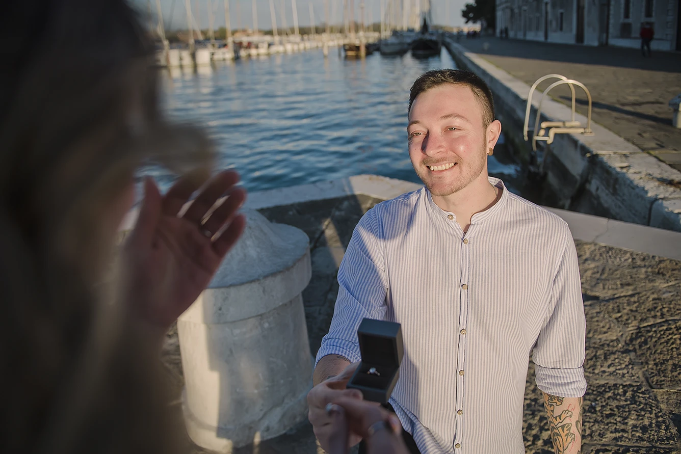 Barth unexpectedly gets down on one knee in San Giorgio Maggiore, presenting an engagement ring to a surprised Maria, whose hands cover a joyful smile.