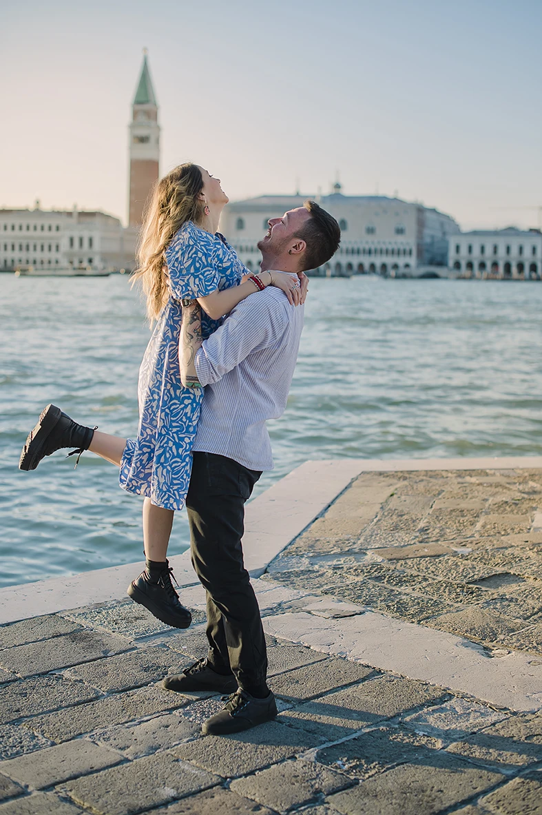 The newly-engaged couple embrace tightly in San Giorgio Maggiore, their expressions a mix of shock and delight.