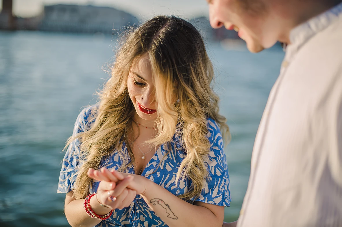 Close-up of Maria's hands as she lovingly touches Barth's shoulder while looking down at the ring with teary eyes of happiness against the backdrop of the Venice lagoon.
