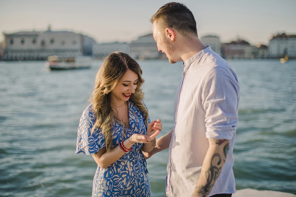 Close-up of Maria's hands as she lovingly touches Barth's shoulder while looking down at the ring with teary eyes of happiness against the backdrop of the Venice lagoon.
