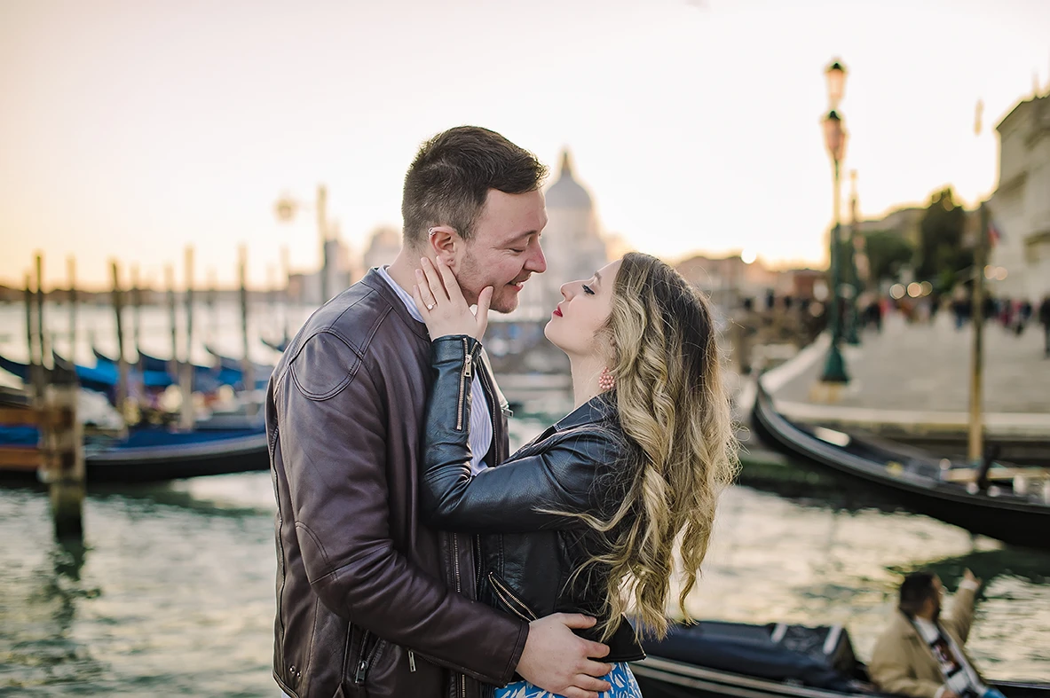 Laughing together, Maria playfully places her engagement ring-adorned hand on Barth's chest as they savor the moment, a gondola leisurely drifting in the background.