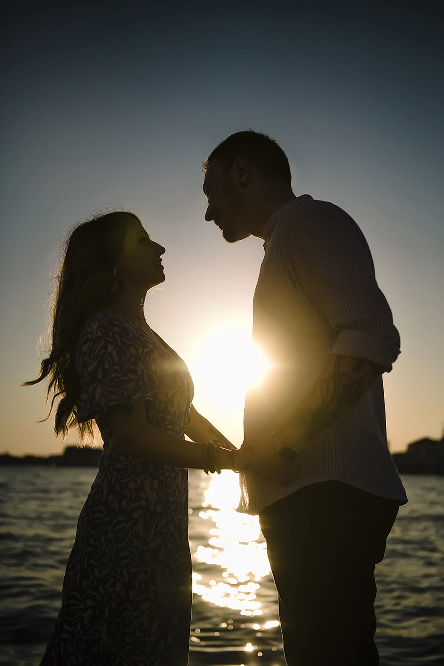 An intimate kiss of Barth and Maria as they stand by the Grand Canal, their silhouettes framed against the twinkling lights of evening Venice
