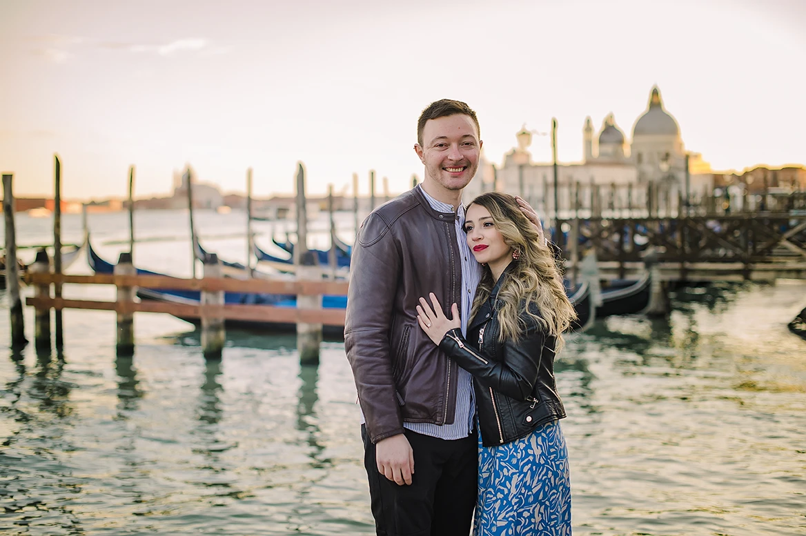 Laughing together, Maria playfully places her engagement ring-adorned hand on Barth's chest as they savor the moment, a gondola leisurely drifting in the background.
