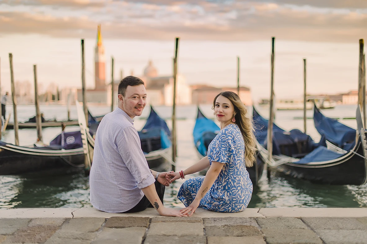 he fiancés share a gentle kiss  with the historic buildings of Venice and boats passing by in the soft, fading light of dusk