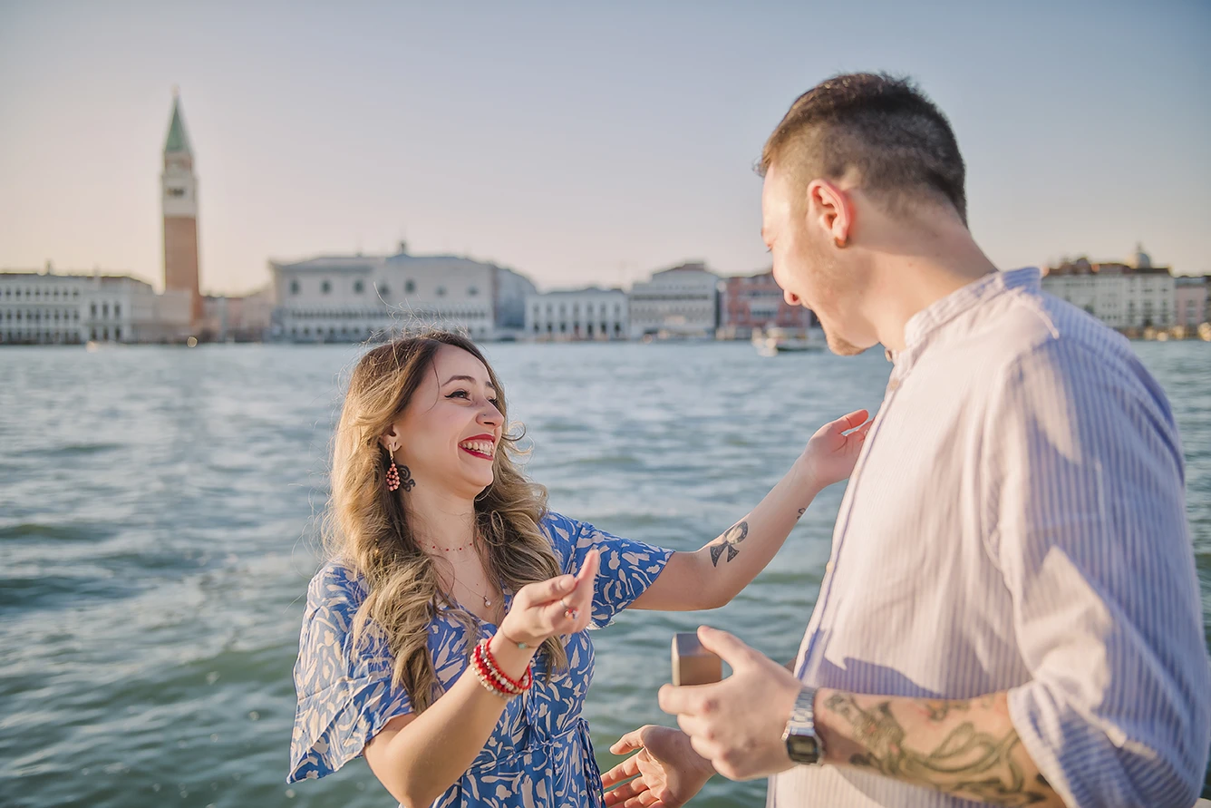 The newly-engaged couple embrace tightly in San Giorgio Maggiore, their expressions a mix of shock and delight.