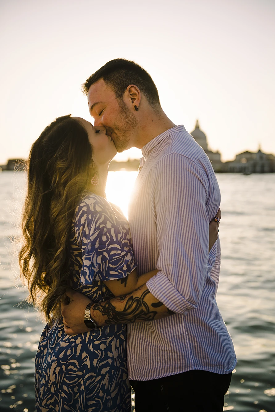 An intimate kiss of Barth and Maria as they stand by the Grand Canal, their silhouettes framed against the twinkling lights of evening Venice