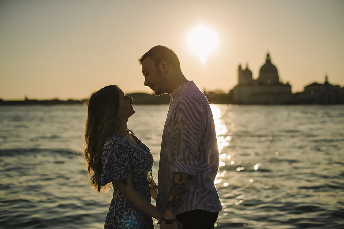 An intimate kiss of Barth and Maria as they stand by the Grand Canal, their silhouettes framed against the twinkling lights of evening Venice