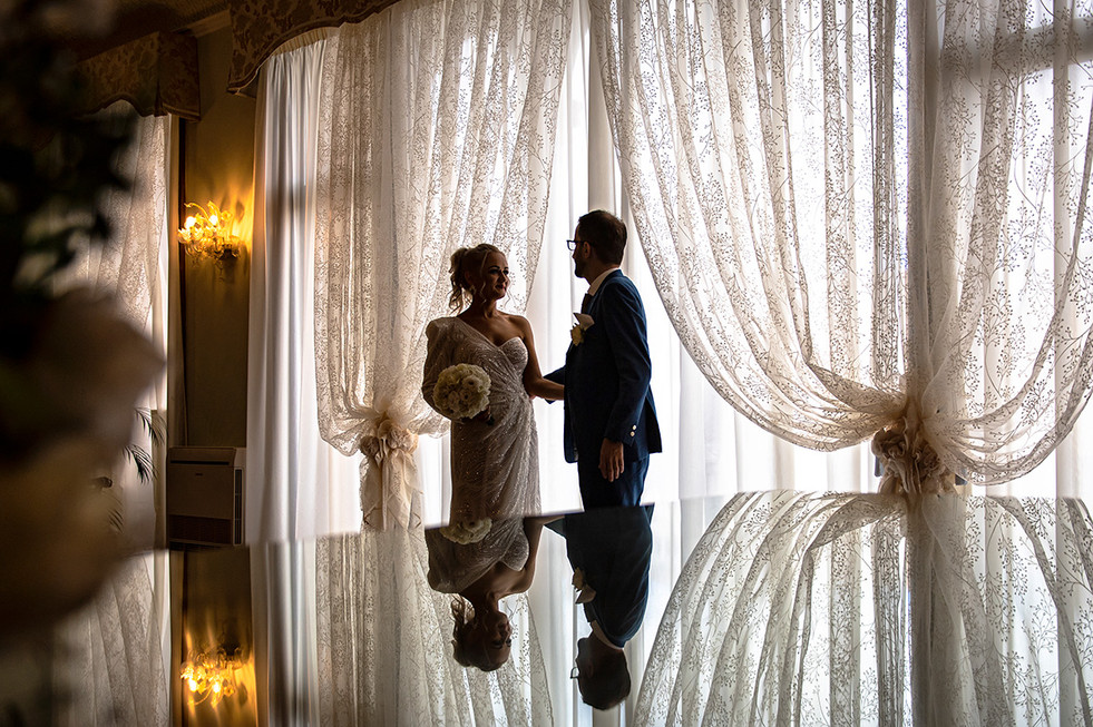 A serene snapshot capturing the essence of Venice: the bride and groom beside the large windows of Palazzo Cavalli with panoramic views of the Grand Canal.