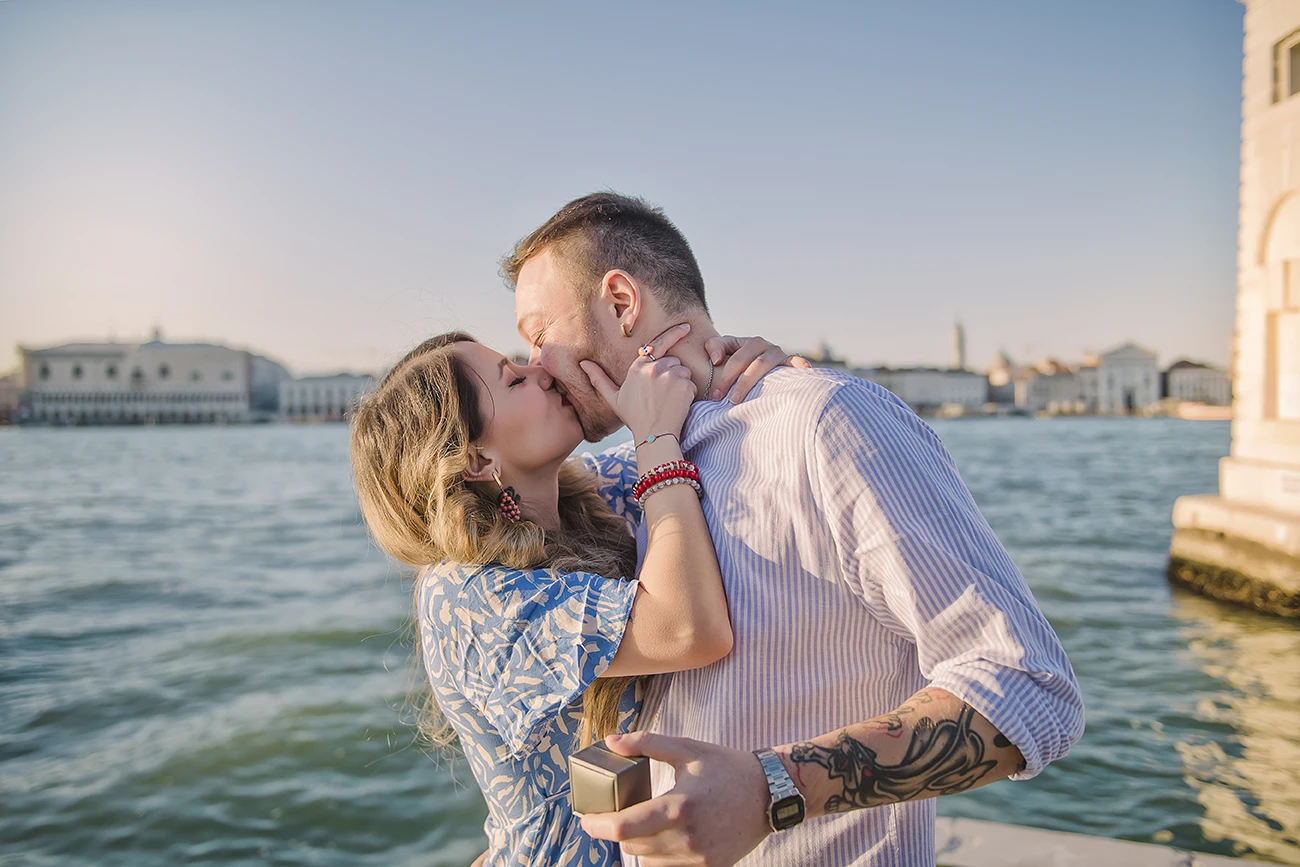The newly-engaged couple embrace tightly in San Giorgio Maggiore, their expressions a mix of shock and delight.