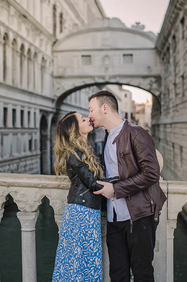 A candid shot capturing the couple's spontaneous dance, with Maria's flowing dress and the serene, amber-tinted sky of Venice creating a timeless scene.