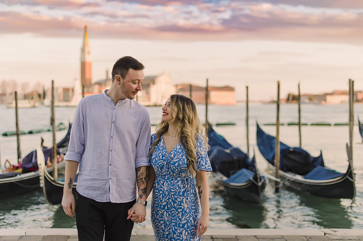 he fiancés share a gentle kiss  with the historic buildings of Venice and boats passing by in the soft, fading light of dusk