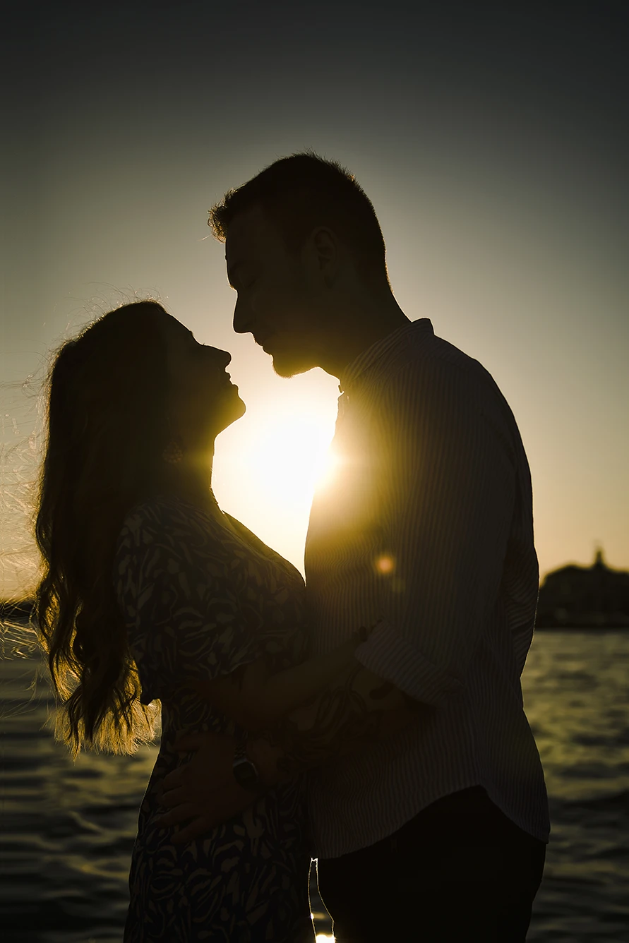 An intimate kiss of Barth and Maria as they stand by the Grand Canal, their silhouettes framed against the twinkling lights of evening Venice