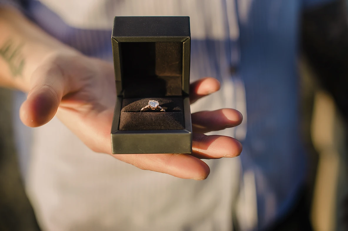 Close-up of Maria's hands as she lovingly touches Barth's shoulder while looking down at the ring with teary eyes of happiness against the backdrop of the Venice lagoon