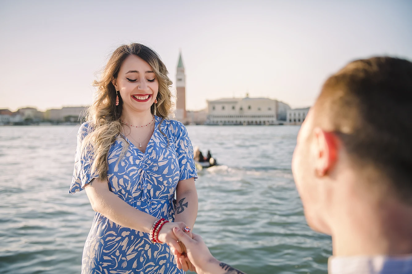 Barth unexpectedly gets down on one knee in San Giorgio Maggiore, presenting an engagement ring to a surprised Maria, whose hands cover a joyful smile.