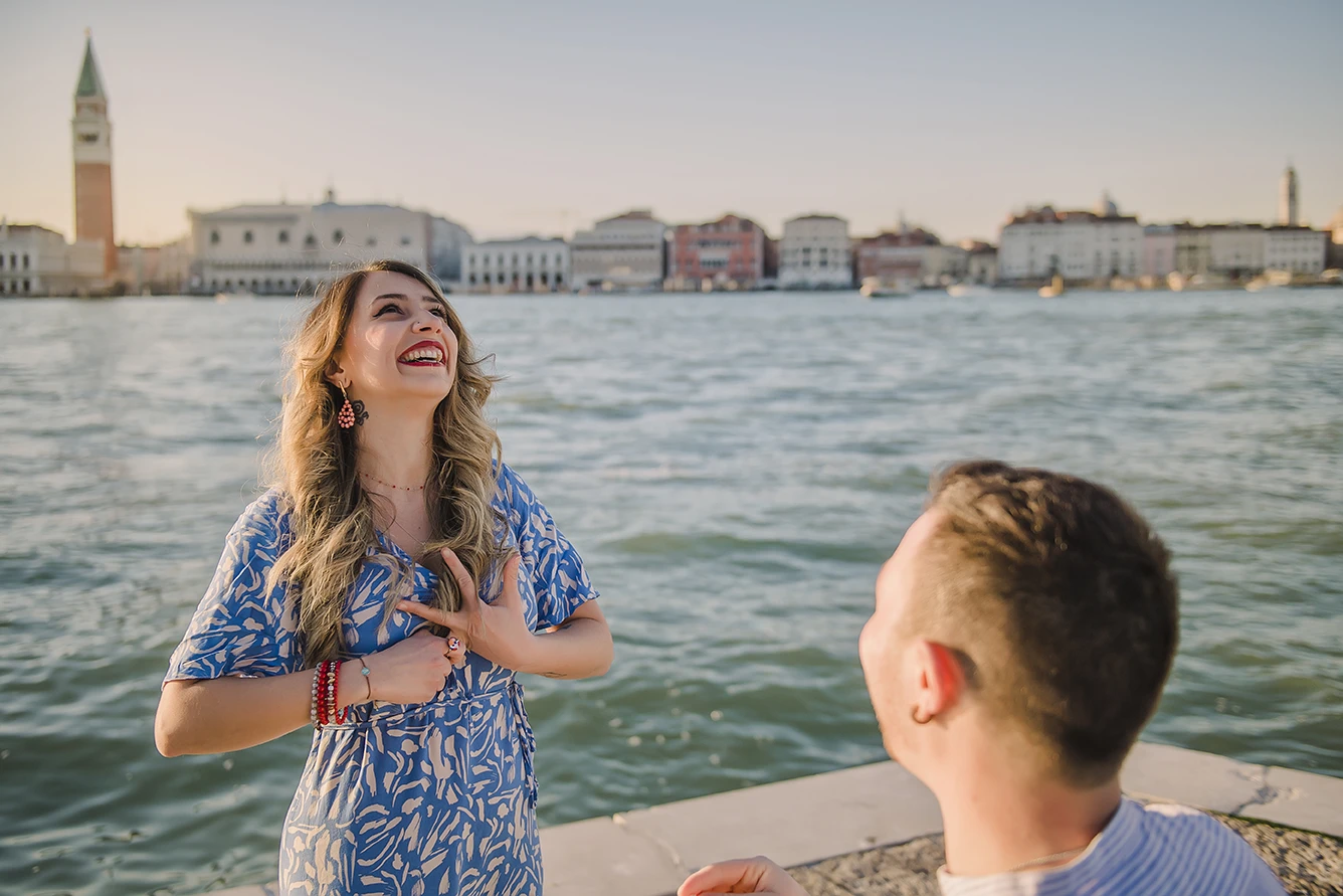 Close-up of Maria's hands as she lovingly touches Barth's shoulder while looking down at the ring with teary eyes of happiness against the backdrop of the Venice lagoon