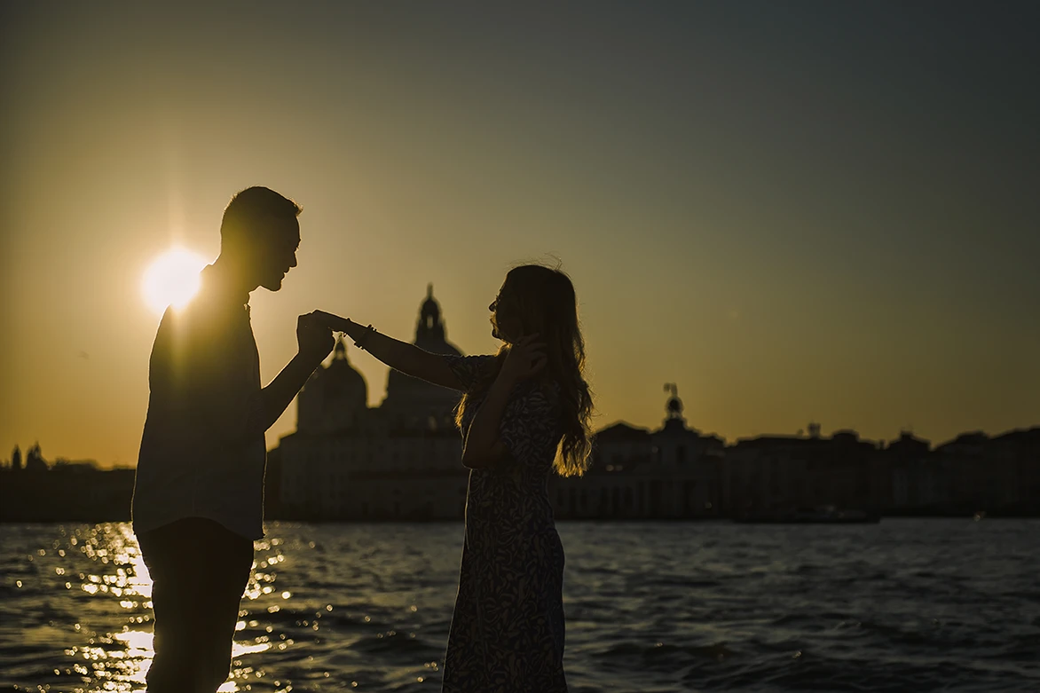 An intimate kiss of Barth and Maria as they stand by the Grand Canal, their silhouettes framed against the twinkling lights of evening Venice