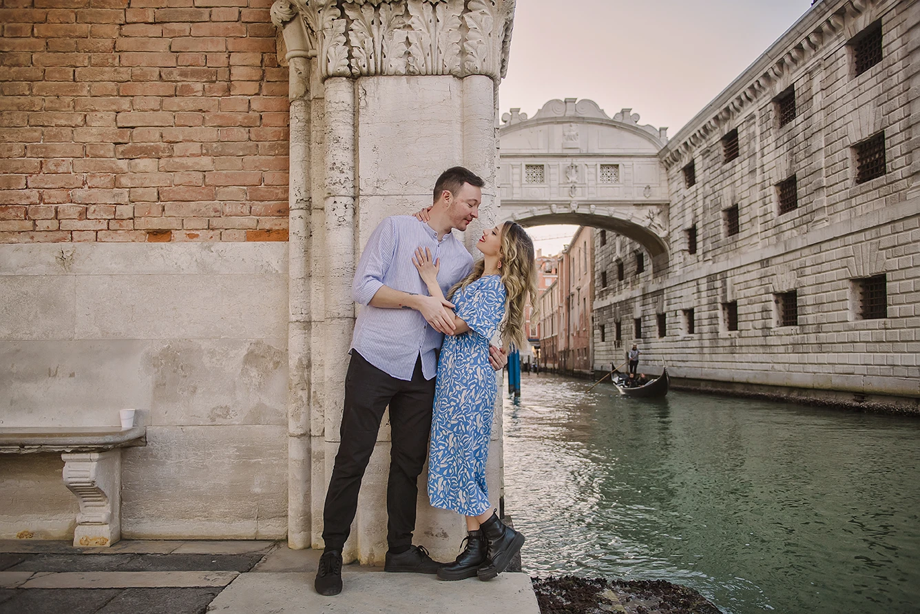 he fiancés share a gentle kiss  with the historic buildings of Venice and boats passing by in the soft, fading light of dusk