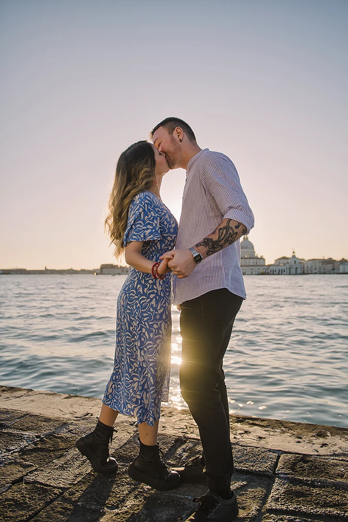 An intimate kiss of Barth and Maria as they stand by the Grand Canal, their silhouettes framed against the twinkling lights of evening Venice