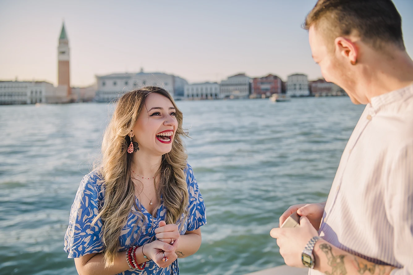 Close-up of Maria's hands as she lovingly touches Barth's shoulder while looking down at the ring with teary eyes of happiness against the backdrop of the Venice lagoon.